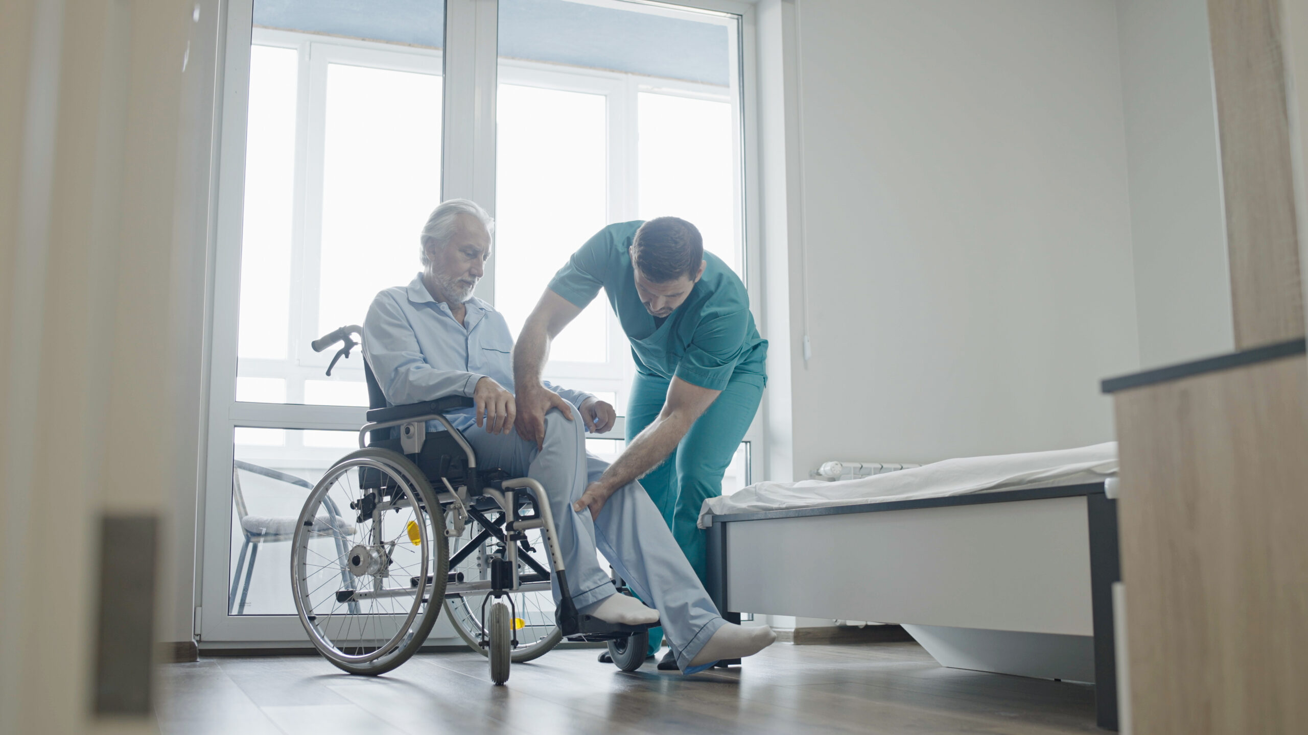 Male nurse helping patient with disability to sit in wheelchair, rehabilitation center